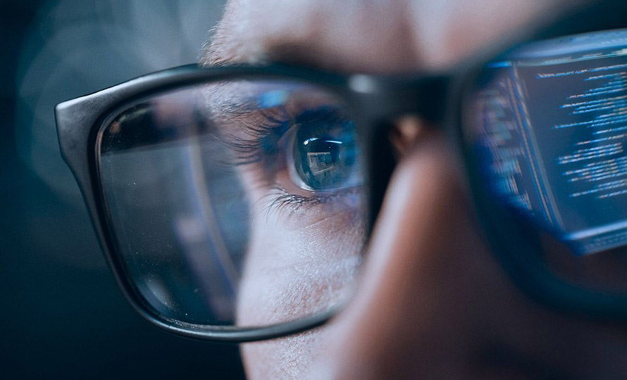 Close-up of person’s eye with computer code reflected in glasses.
