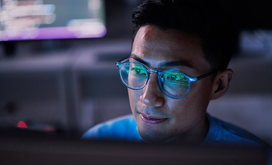 IT professional working at a computer with code reflected in glasses.