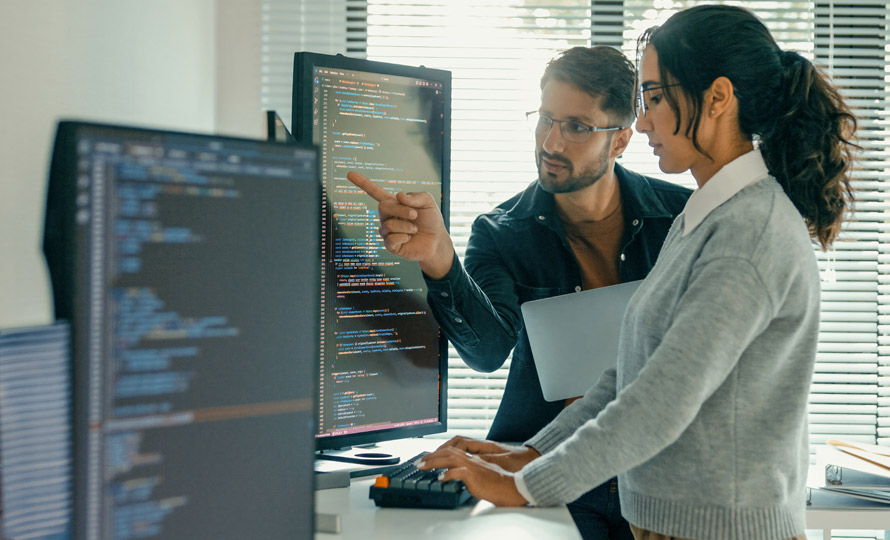 Two professionals reviewing code on a large monitor in a modern office.
