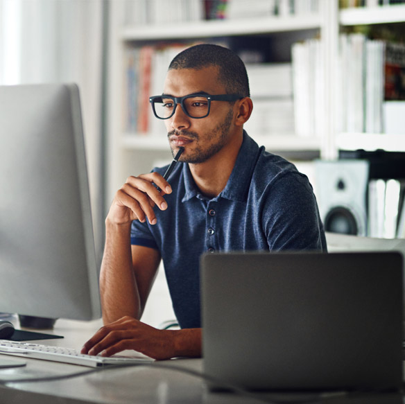 Man working at a desk with a desktop computer and laptop in a modern office setting.