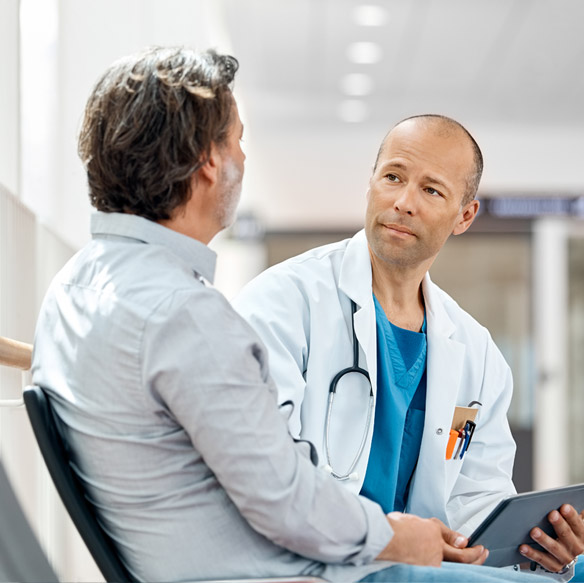 Doctor speaking with a patient in a hospital hallway, holding a digital tablet.