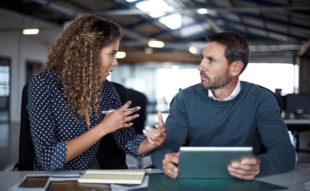 Two professionals discussing ideas while working with a tablet in an office.