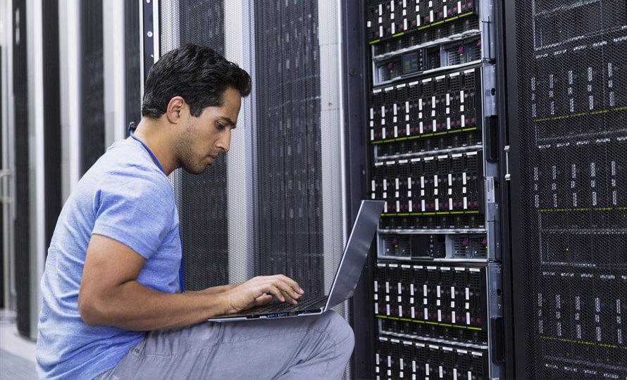 IT professional working on a laptop while managing server racks in a data center.