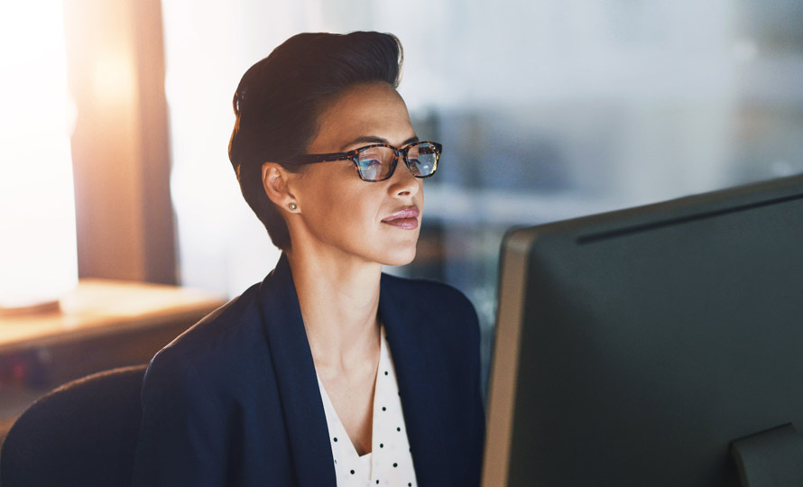 Professional woman in glasses working at a computer in an office setting.