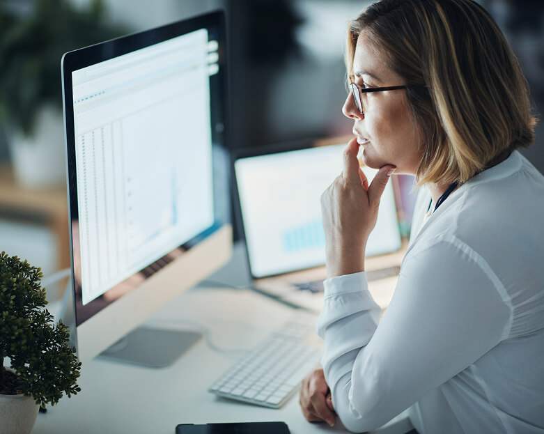 Woman reviewing data charts on a computer monitor in an office setting.